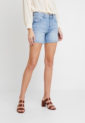 Shorts en denim bleu clair avec une coupe classique, cinq poches et une finition légèrement délavée. Associés à des sandales à talons à brides marron.