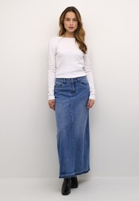 Falda larga de mezclilla azul con un ligero vuelo, cintura alta, dos bolsillos frontales y un dobladillo limpio. Combinada con una blusa ajustada de manga larga blanca.
