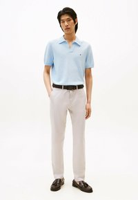 Polo shirt azzurro chiaro a maniche corte con superficie texturizzata, abbinato a pantaloni grigi chiari e mocassini marroni scuri, con una cintura nera.