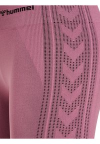 Gros plan sur des leggings de sport roses texturés avec un motif chevron noir et le logo "hummel" près de la taille.