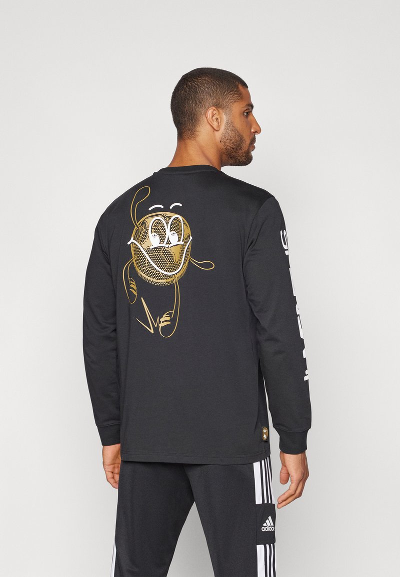 Camiseta negra de manga larga con gráfico de dibujos animados dorado en la parte posterior, con un diseño de malla. Texto blanco en la manga. Material de algodón suave.