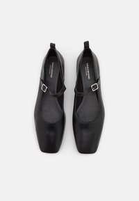 Pantofi din piele neagră cu un design pătrat al vârfului, având o parte frontală largă, curea ajustabilă pentru glezne și căptușeală interioară texturat�ă.