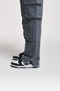 Pantaloni cargo gri cu multiple buzunare, fermoare la tiv, asortați cu adidași alb-negru cu vârf perforat și design cu șireturi.