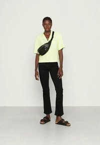Camisa verde clara de mangas curtas, calças pretas ajustadas, bolsa preta de ombro e sandálias pretas. Tecido suave e corte descontraído.