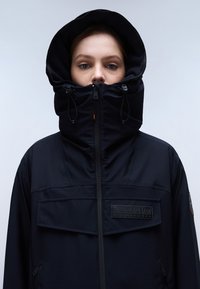 Giacca nera isolante con colletto alto, cappuccio grande e chiusure con zip. Presenta un tessuto testurizzato e una toppa con logo sul petto.