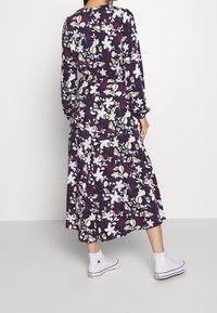 Květinové midi šaty s dlouhými rukávy, s tmavě fialovým základem a bílými, růžovými a oranžovými květy. Stylizované s bílými teniskami na vysoké podešvi.