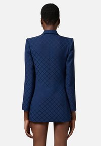 Blazer blu navy con un motivo a diamante texturizzato, maniche lunghe, taglio sartoriale e una fessura posteriore singola. Tessuto liscio e spalle strutturate.