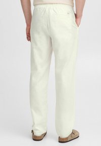 Witte linnen broek met een elastische tailleband, voorzien van een achterzak en een relaxed fit, gecombineerd met lichtbruine instapschoenen.