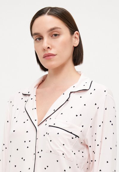 Ροζ πιτζάμα κορυφή με μαύρο σχέδιο καρδιάς, κουμπωτή κλείσιμο, τσέπη με μαύρο περιθώριο και γιακά. Μαλακό ύφασμα με απαλό τελείωμα.