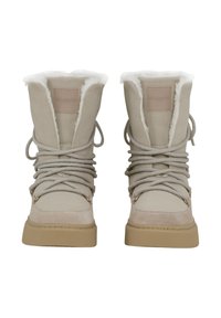 Beige suède laarzen met een bontvoering, ronde neuzen en vetersluiting. Heeft een tan rubberen zool en een klein logopatch aan de voorkant.