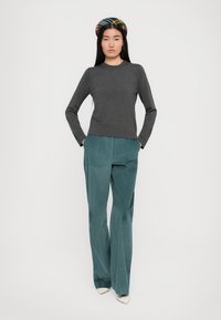 Un top gri cu mânecă lungă, fabricat dintr-un material moale, asociat cu pantaloni largi din bumbac ribatat de culoare teal. Pantofii albi cu vârful ascuțit și o bandă de păr cu model completează ținuta.