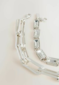 Bracelet en chaîne en argent avec des maillons allongés s'entrelacés et des pierres rectangulaires transparentes serties dans des accents métalliques. Fini lisse et poli.