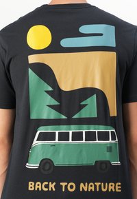 Sort T-shirt med multicoloreret grafik: grøn varevogn, gul sol, abstrakte bjerge, og "BACK TO NATURE" i fed gul tekst.