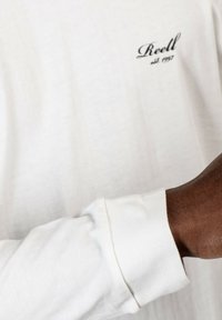 Weißes Langarmhemd mit schmalem Bund, versehen mit einem kleinen schwarzen gestickten "Reell"- und "est. 1997"-Logo auf der Brust. Weiche Textur.