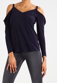 Mörk marinblå långärmad topp med kall axeldesign, V-ringning, mjukt material och lös passform, tillsammans med grå åtsittande jeans.