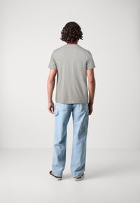 T-shirt en coton gris à col rond et manches courtes, associé à un jean en denim bleu clair ample avec poches latérales.