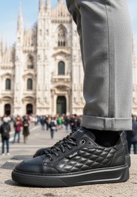 Czarne pikowane skórzane sneakersy z okrągłym noskiem, czarnymi sznurówkami i grubą czarną gumową podeszwą, zestawione z szarymi zwężanymi spodniami.