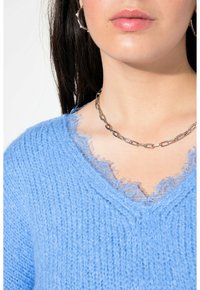 Sweater en maille bleu clair avec un col en V aux bords effilochés, superposé d'une délicate garniture en dentelle. Un collier en chaîne argenté apporte du contraste.