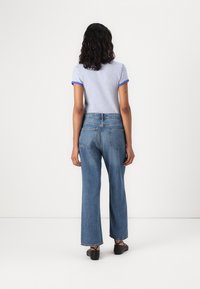 Camisa de manga curta ajustada, azul e branca às riscas, calças de ganga azuis de cintura alta e pernas largas, combinadas com sapatos pretos, vista de costas.