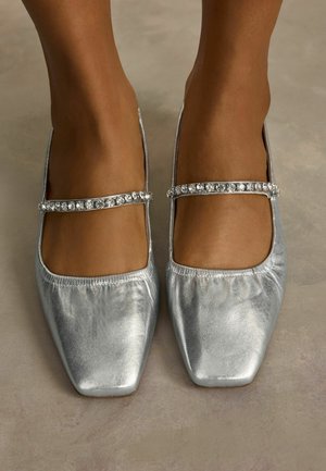 Hopeisia ballerina-kenkiä, joissa on sileä metallinen pinta, nelikulmainen kärki ja koristeltu kimaltavalla strassihihnalla jalkapöydän kohdalla.