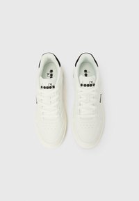 Par de ténis brancos da Diadora com atacadores, logótipo preto na língua e forro interior do calcanhar preto, exibidos em vista superior sobre fundo branco.