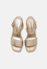 Sandales en satin doré avec deux larges sangles et une boucle à la cheville. Semelle intérieure rembourrée et détails en bord tressé, conçues pour le confort et le style.