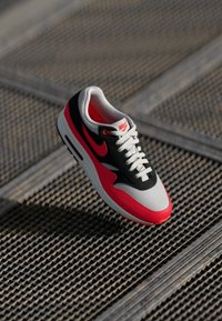 Adidașii Nike Air Max cu un superior din plasă și suede în nuanțe de negru, roșu și gri, cu șireturi albe și sistem de amortizare vizibil în talpă.