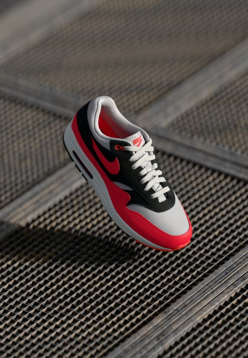 Adidașii Nike Air Max cu un superior din plasă și suede în nuanțe de negru, roșu și gri, cu șireturi albe și sistem de amortizare vizibil în talpă.