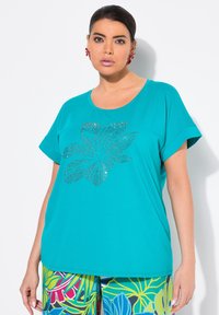 Camiseta de manga corta turquesa con escote redondo que presenta un diseño floral de strass plateado. Tejido suave con un ajuste relajado.