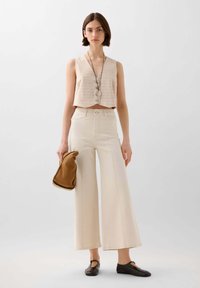 Beige cropped vest met verticale strepen, hooggewaisted crèmekleurige wijde broek, bruine tas en donkere schoenen met een subtiele uitstraling.