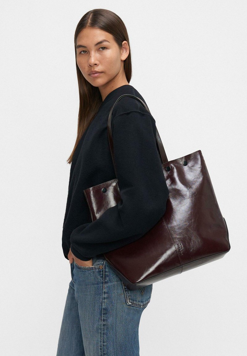 Burgundowa skórzana torba na ramię o gładkiej fakturze i wypolerowanym wykończeniu. Posiada dwa górne uchwyty oraz usztywniony kształt.