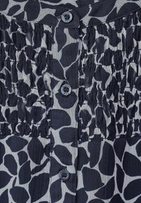 Schwarz-weiße Bluse mit einem Blättermuster, gerüschtem Textur und zwei Knöpfen an der Knopfleiste. Leichter Stoff mit einer weichen Haptik.