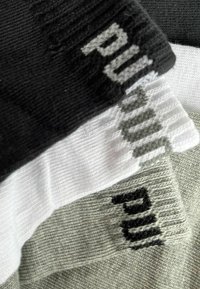 Drei Paar Socken in Schwarz, Weiß und Hellgrau, mit gerippter Textur und dem auffälligen "PUMA"-Logo, das in jeder Farbe eingewebt ist.