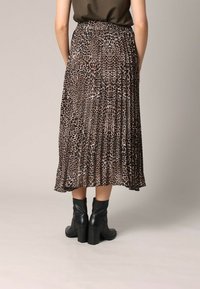 Jupe maxi plissée imprimée animal dans des tons de noir et brun. Fabriquée en tissu léger, associée à des bottines à talons noires.