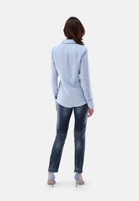 Light blue long-sleeve shirt with a collared neckline, paired with dark denim jeans, and light blue high-heeled shoes.
