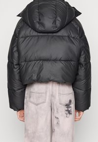 Czarna pikowana kurtka puchowa z kapturem, z przeszyciami, grubym wypełnieniem i elastycznymi mankietami, zestawiona z jasnoróżowymi, postrzępionymi dżinsami.