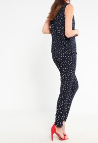 Ensemble marine en deux pièces comprenant un top sans manches à motif à pois, associé à un pantalon slim, le tout complété par des chaussures à talons rouges.