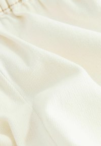 Tissu doux de couleur blanc cassé avec une texture côtelée subtile et des plis délicats, mettant en valeur le matériau textile et les détails de couture.