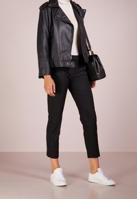 Svart läderbikerjacka med silverdragkedjor, figursydd vit polotröja, skräddarsydda svarta byxor och vita sneakers. Svart handväska ingår.