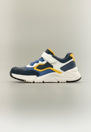 Baskets de sport pour enfant avec des empiècements bleus, blancs et jaunes, semelle blanche, lacets bleus et bride velcro blanche sur fond uni.