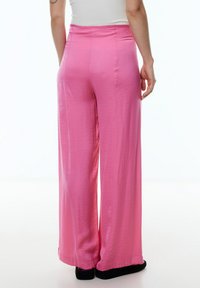 Weite Hosen aus glattem, leichtem Material in leuchtendem Pink. Sie haben eine hohe Taille und eine dezente Textur, ohne sichtbare Taschen.