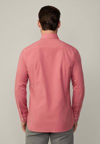 Camisa de manga larga, abotonada, de algodón en rosa claro, con yugo en la parte posterior, puños de un solo botón y dobladillo en forma de camisa.