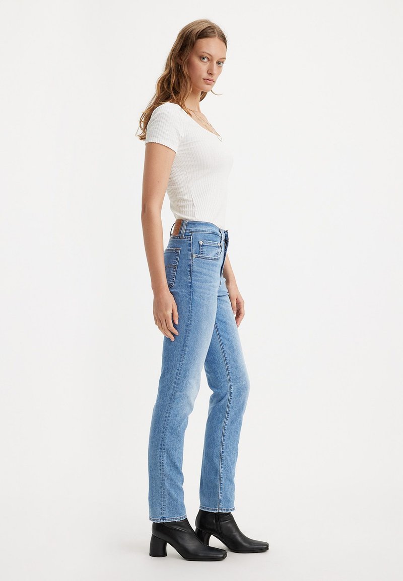 Jean en denim bleu clair avec une coupe droite, associé à un haut ajusté en coton côtelé blanc et des bottines à talons noires.