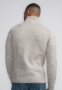 Maglione lavorato a maglia grigio chiaro con colletto alto, motivo testurizzato e orlo a coste, che mostra un design aderente con dettagli sulle cuciture laterali.