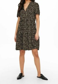 Robe à manches courtes imprimé léopard noir et beige, avec un décolleté en V et une jupe évasée. Associée à des chaussures noires sans lacets.