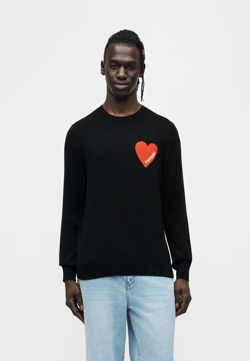 Pull en tricot noir à manches longues, avec un emblème en forme de cœur rouge sur la poitrine gauche portant le mot "FUTURE" en blanc.
