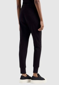 Zwarte sweatpants met een geribbelde tailleband, taps toelopende benen en opgerolde enkels, gecombineerd met gestructureerde zwarte sneakers met een witte zool.
