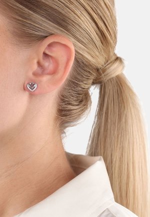 Des boucles d'oreilles en forme de cœur en ton argenté présentent une pierre centrale foncée entourée de petites pierres claires, serties dans une base en métal poli.