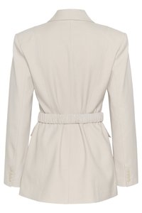 Lys beige skreddersydd blazer med innsnørt midje, lange ermer og glidelås. Glatt stoff med strukturerte sømmer og knappdetaljer.