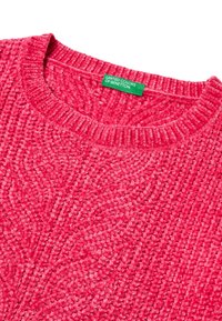 Růžový texturovaný svetr s žebrovaným výstřihem a zelenou značkovou visačkou od United Colors of Benetton na límci.